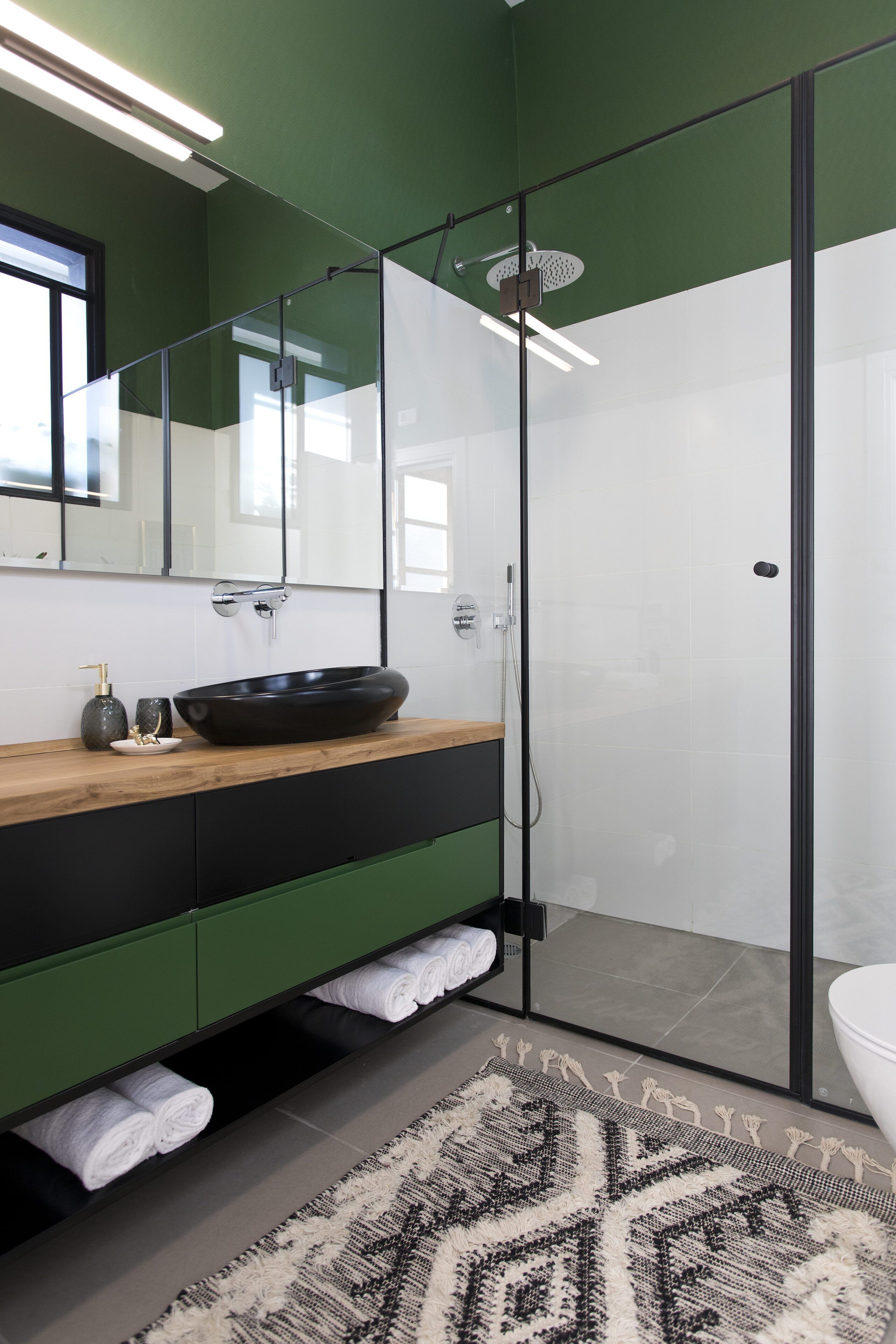 A modern bathroom with a glass-enclosed shower, a wooden vanity with a black sink, and a green cabinet.