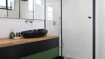 A modern bathroom with a glass-enclosed shower, a wooden vanity with a black sink, and a green cabinet.
