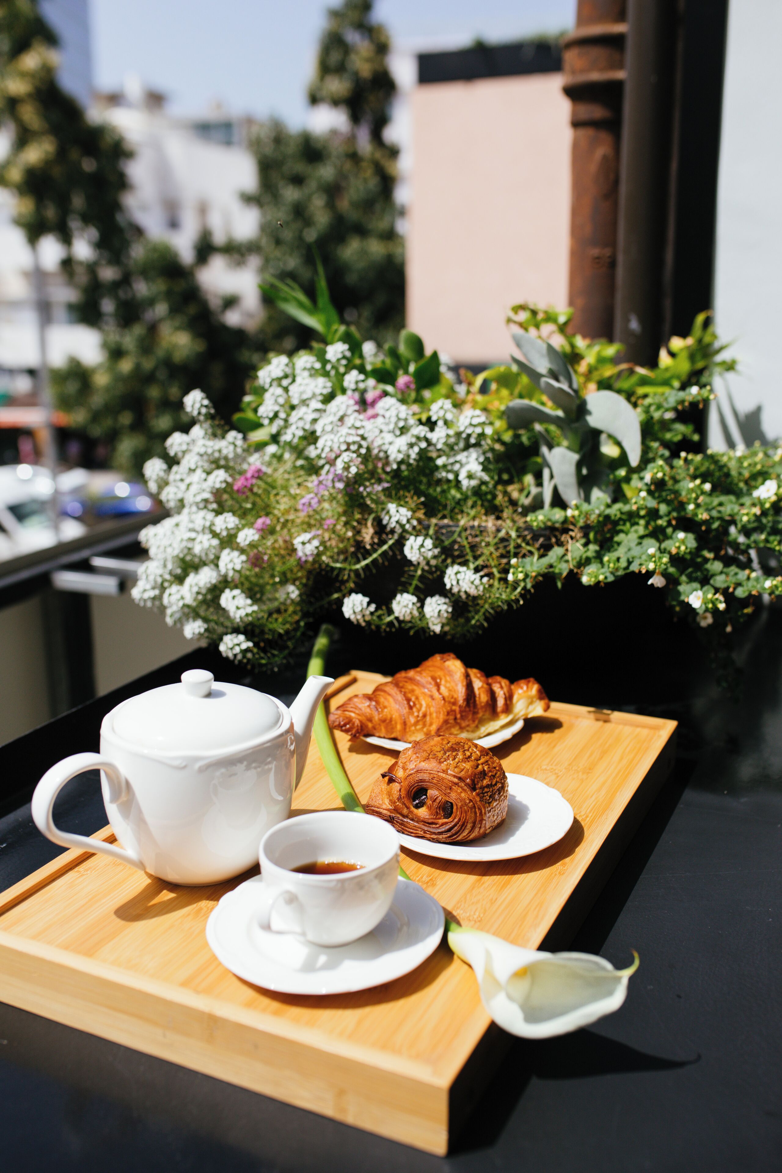 A tray with a teapot, cup, croissant, and a flower on a table.