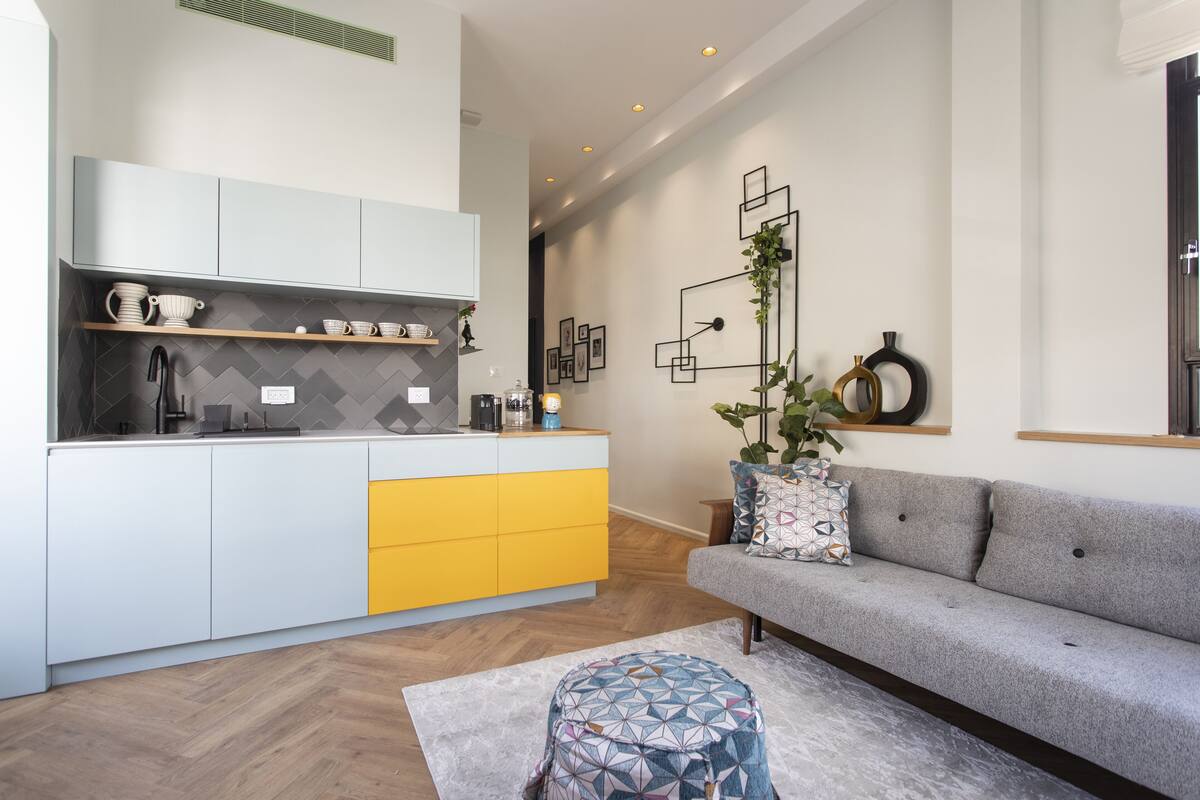 A modern kitchen with a central island, a grey sofa, and a patterned ottoman.