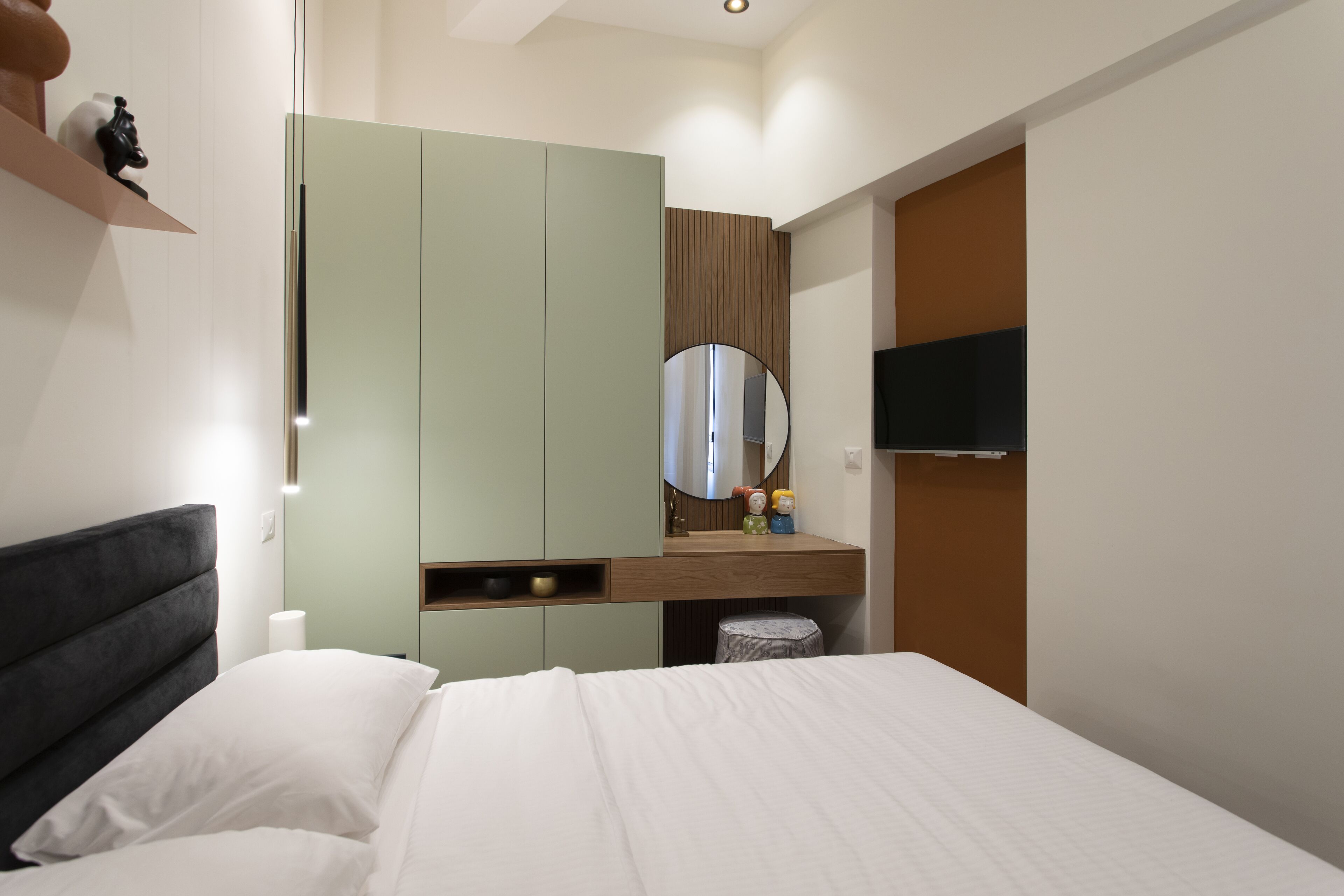 Een slaapkamer met een bed, een garderobe, een kaptafel met spiegel en een televisie aan de muur.