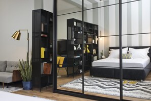 A modern bedroom with a bed, a large black bookshelf, a grey sofa, and a potted plant. - De Picciotto Suites (Tel Aviv)