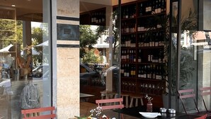 Een openluchtcafé met rode stoelen en tafels, een glazen wand en een zichtbare wijnrek door het glas.