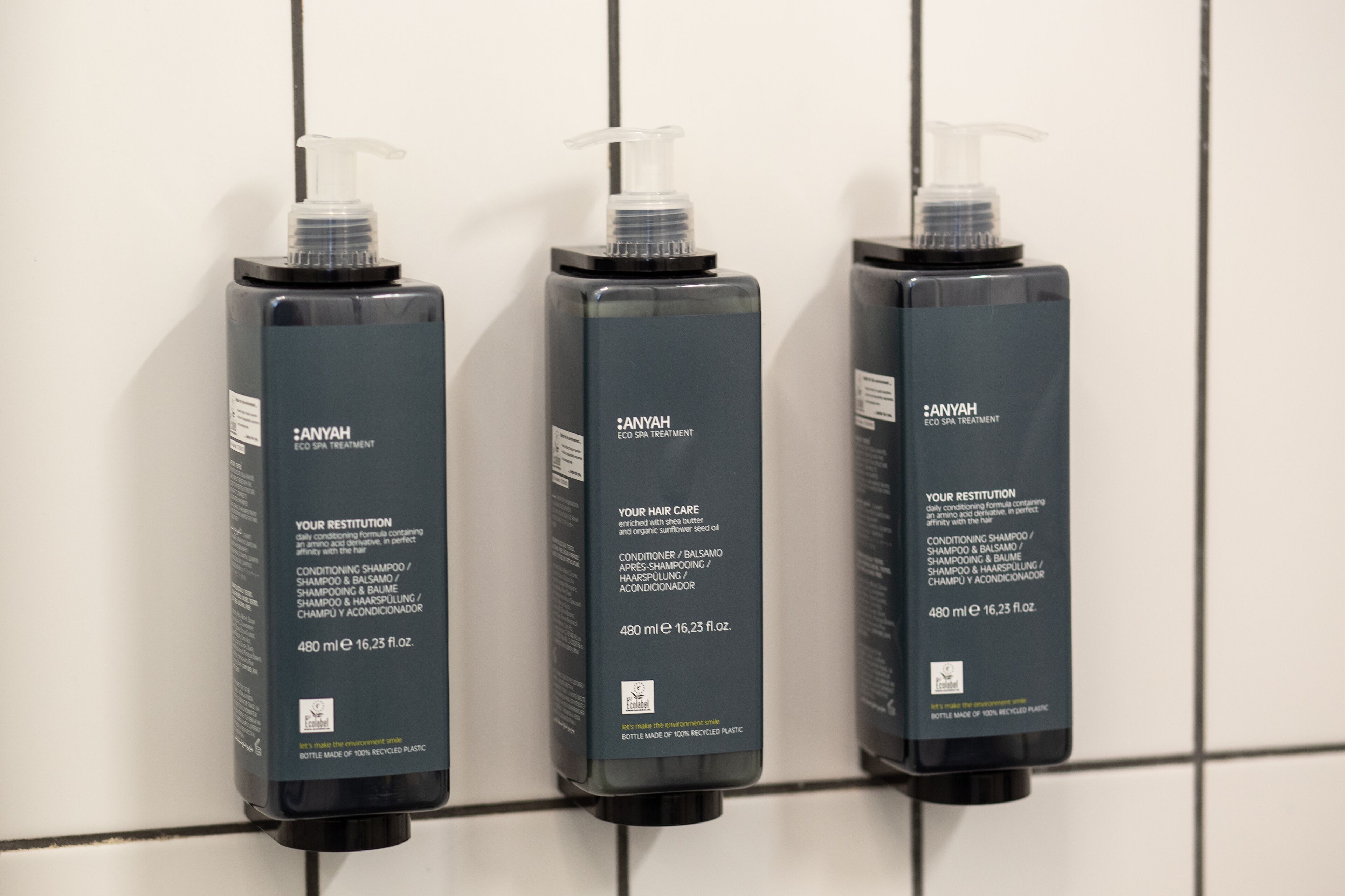 Three bottles of Anyah hair care products mounted on a tiled wall.