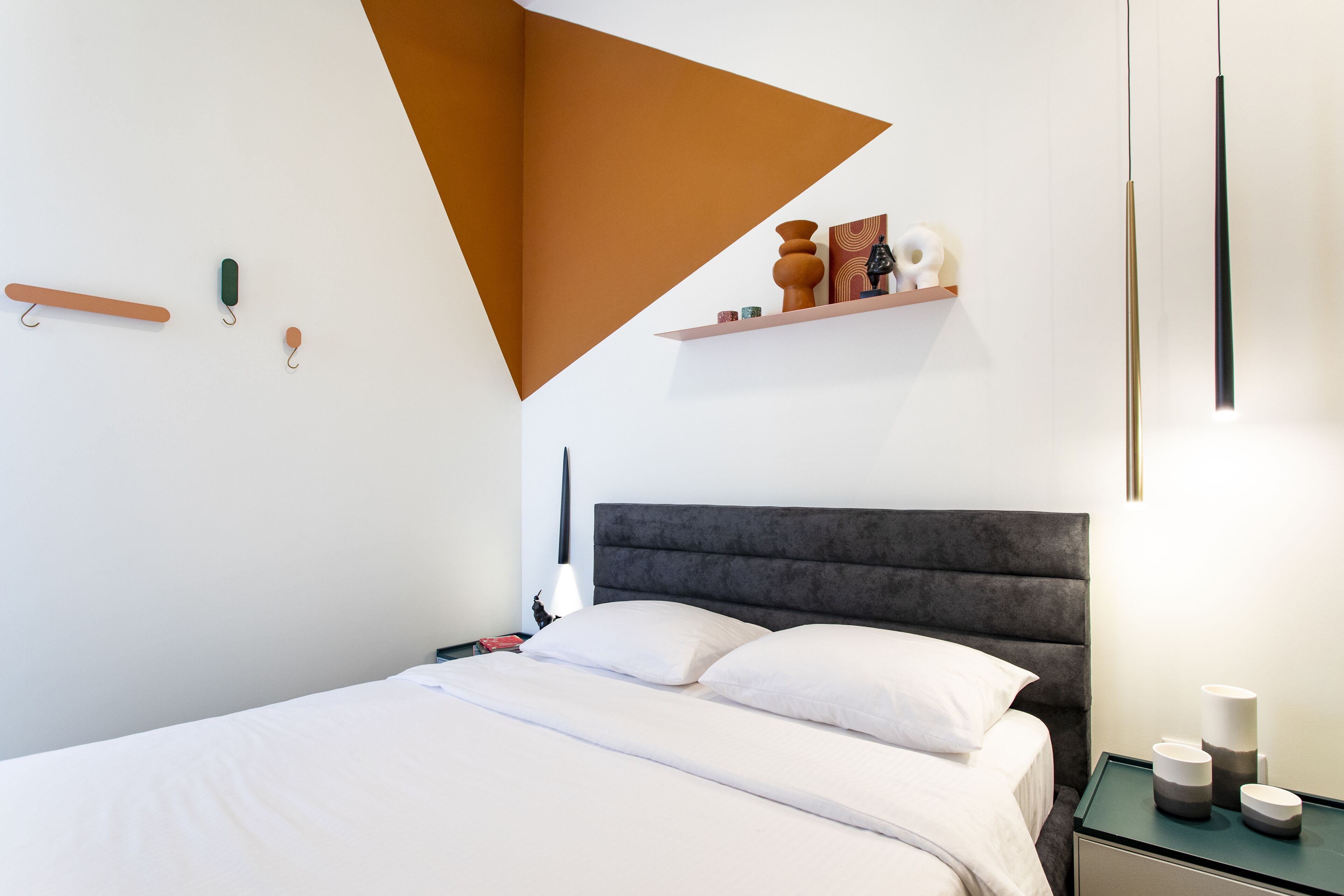 A modern bedroom with a bed, bedside tables, a nightstand, and a wall-mounted shelf with decorative items.
