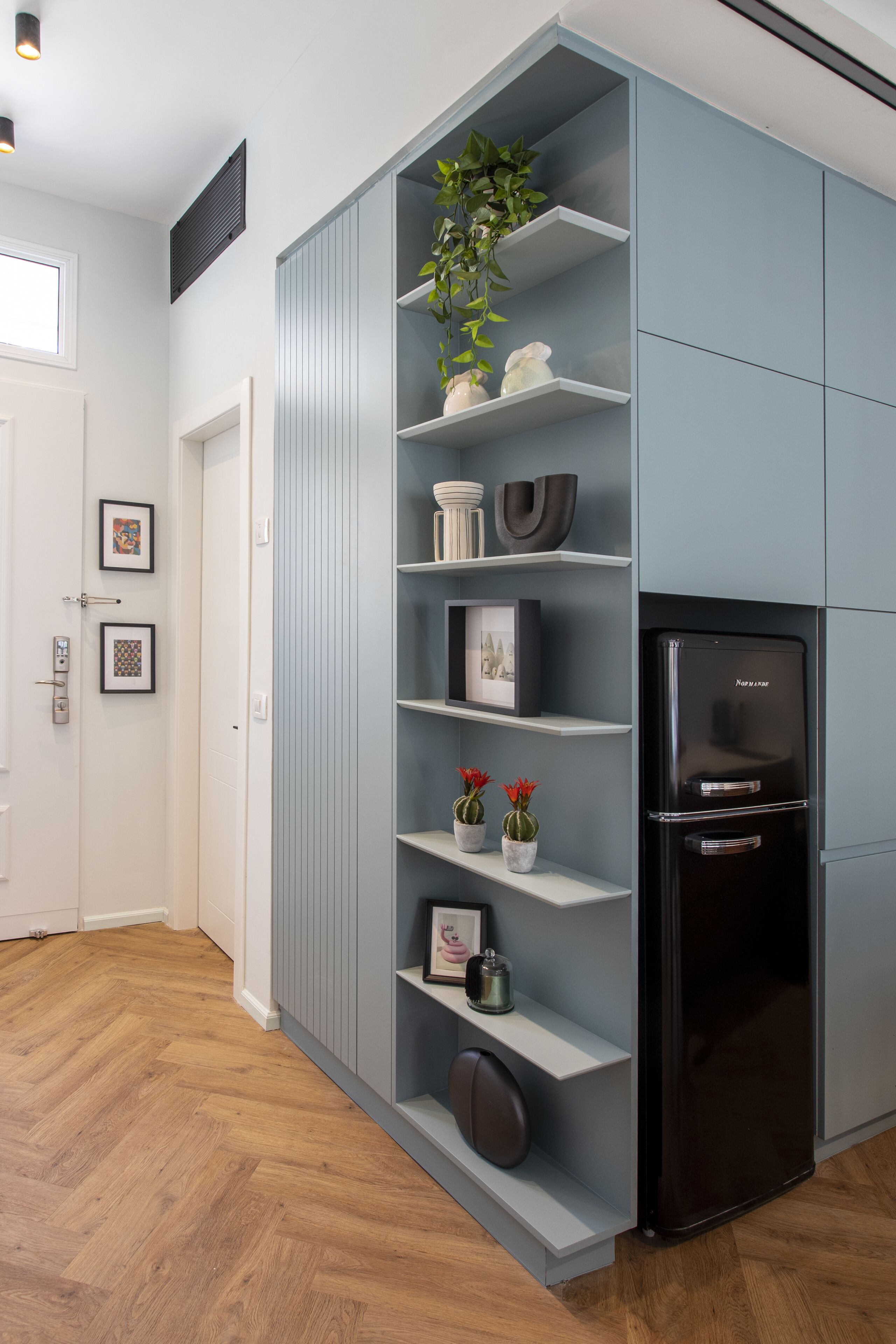 A modern kitchen with built-in shelves, a black refrigerator, and a potted plant.