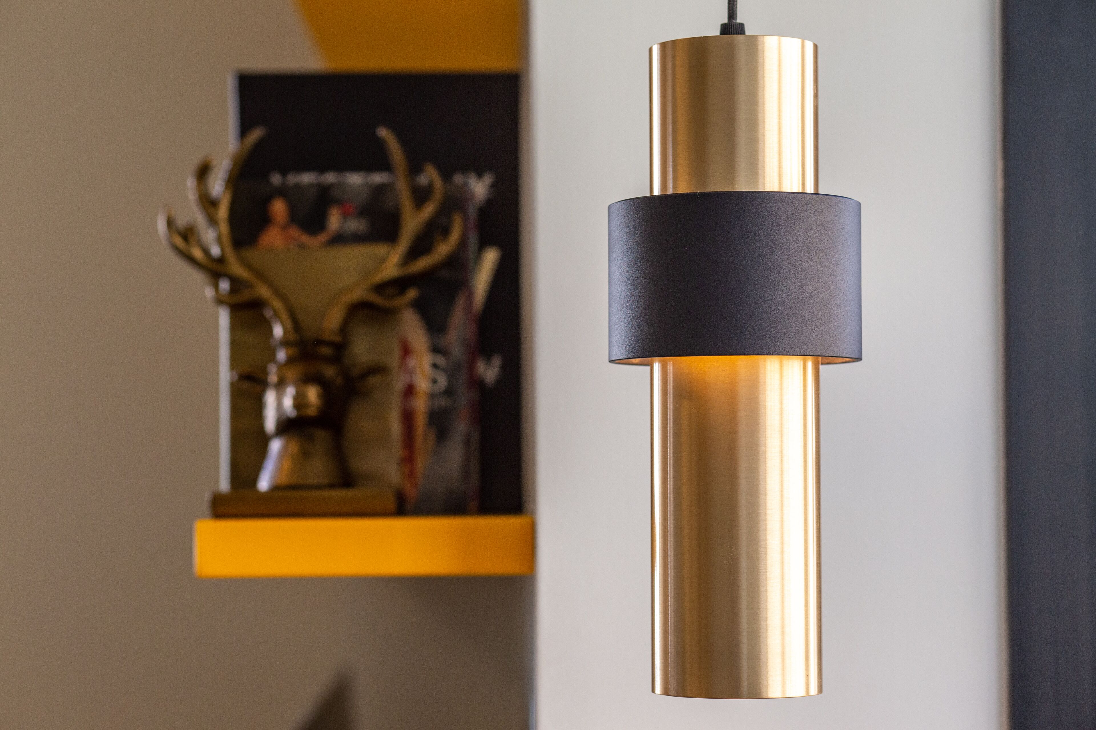 A modern pendant light fixture with a cylindrical gold base and a black cylindrical shade.