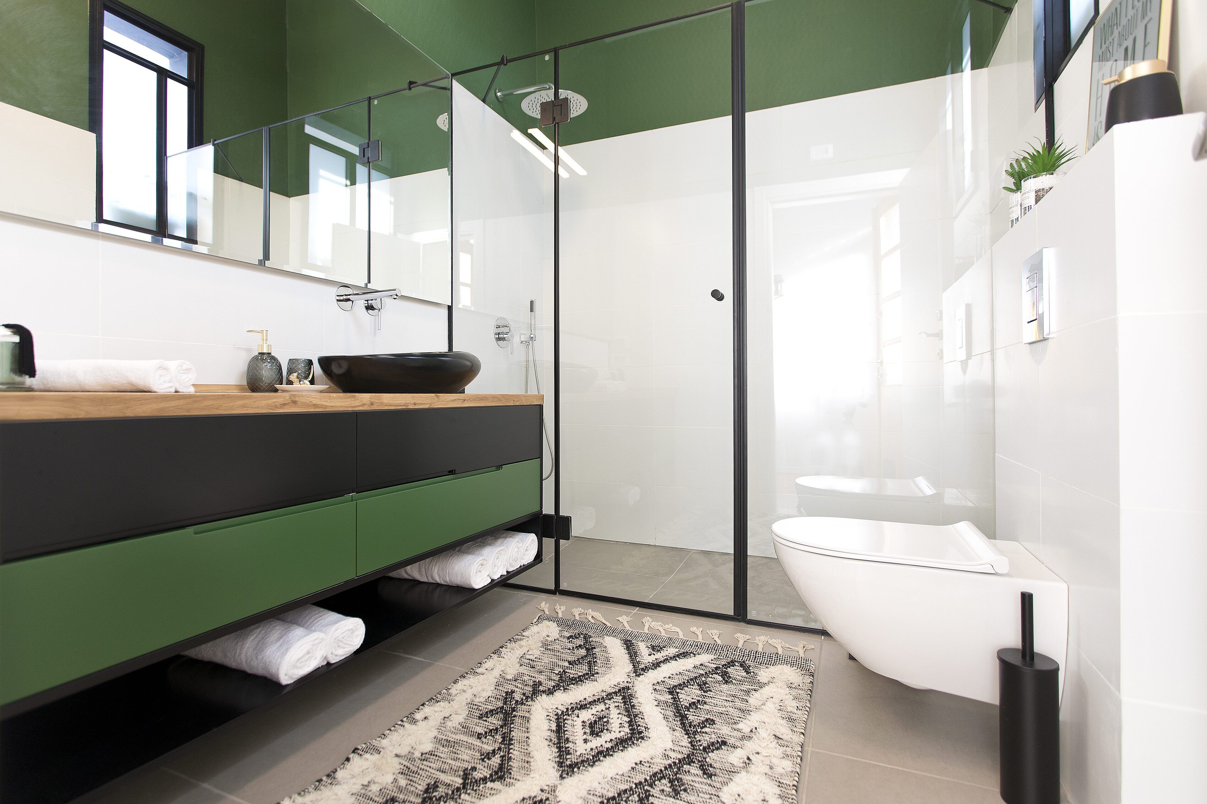 A modern bathroom with a glass shower enclosure, a white sink, and a green vanity.