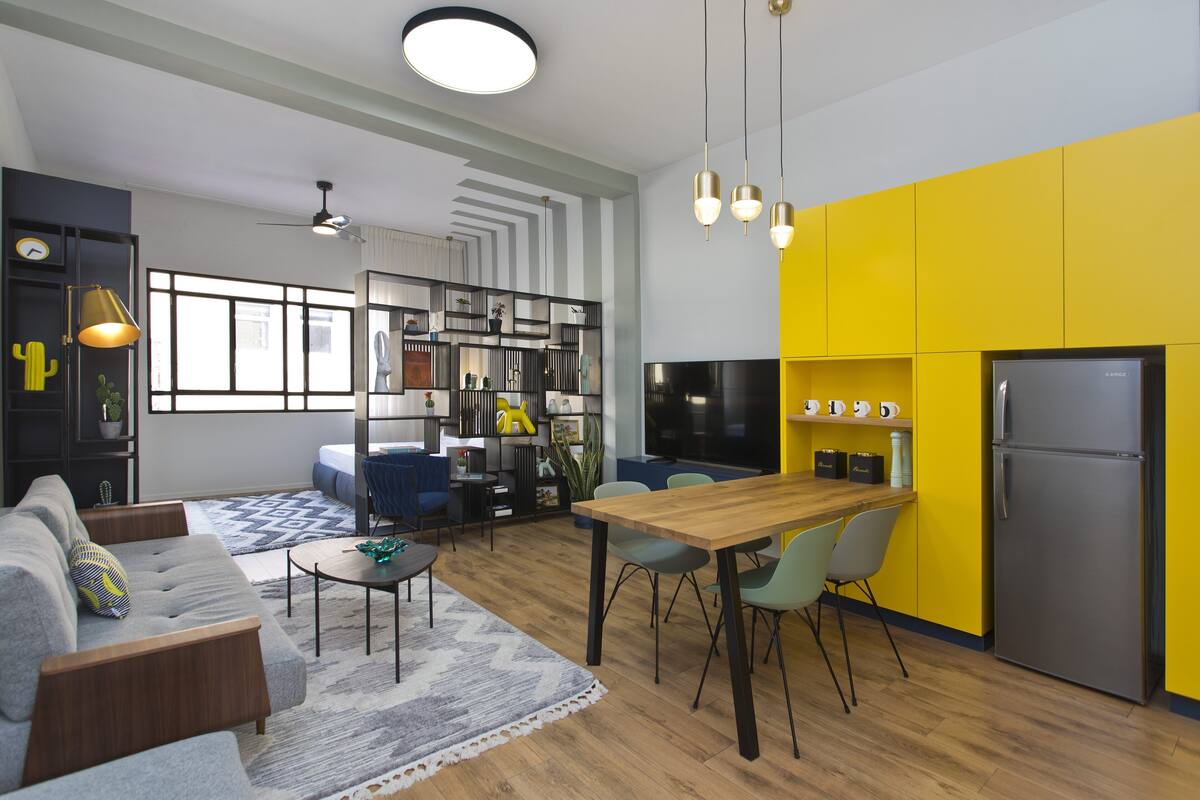A modern kitchen with a dining area, yellow cabinets, and a large TV.