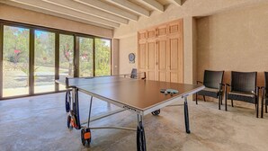 Una sala spaziosa con un tavolo da ping pong, ampie finestre, mobili in legno e poltrone in vimini.
