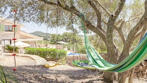 Un'amaca legata tra due alberi in un giardino con piscina e mobili da esterno.