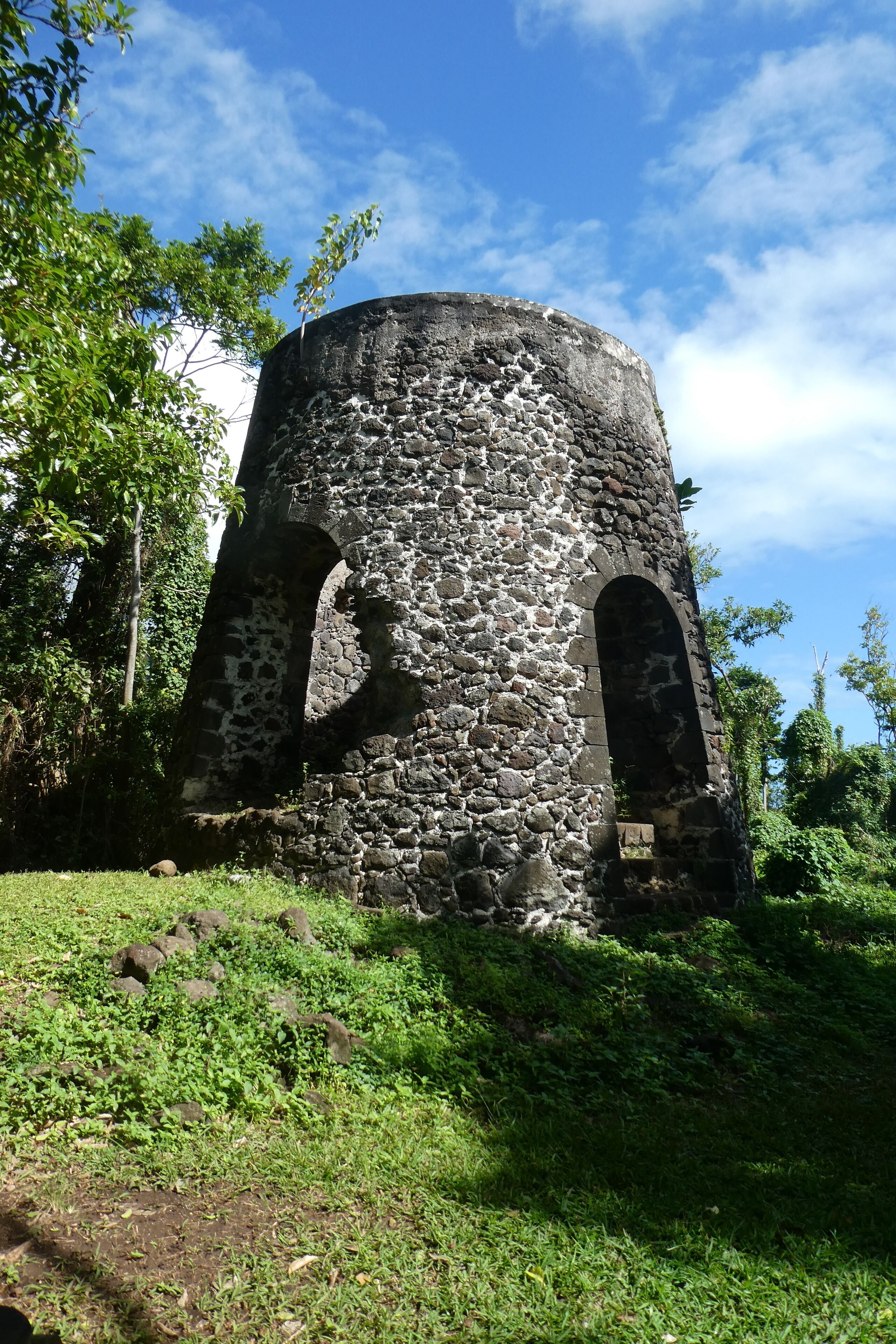 A stone tower with arched openings, surrounded by greenery.