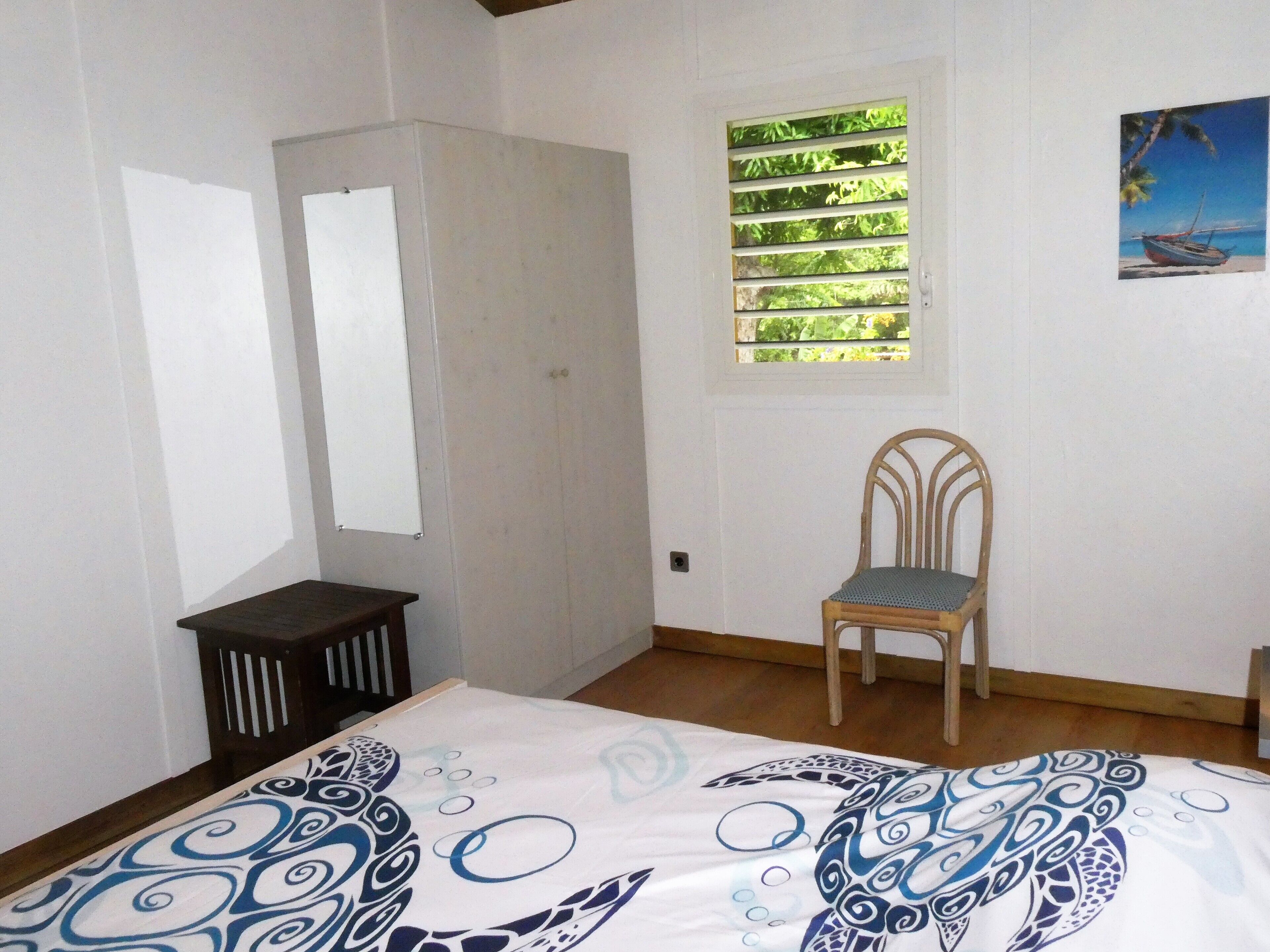 A bedroom with a bed, a chair, a wardrobe, a window with blinds, and a painting on the wall.