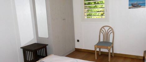 A bedroom with a bed, a chair, a wardrobe, a window with blinds, and a painting on the wall.