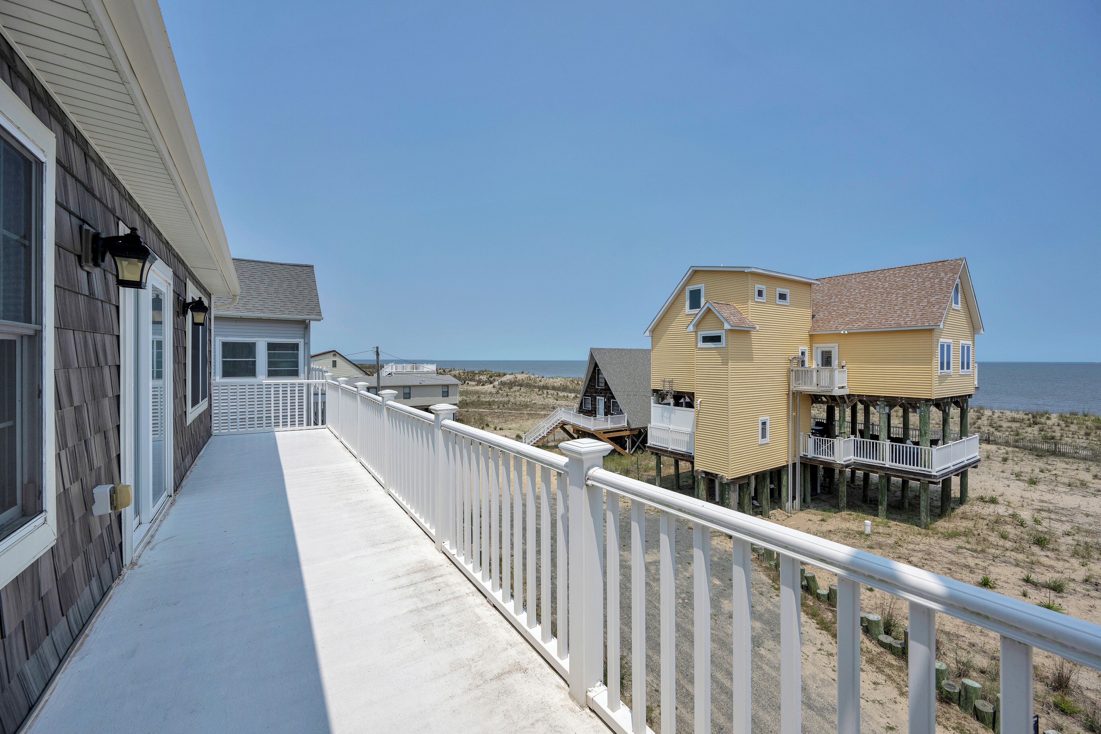 A beachfront property with a covered walkway and multiple buildings, including a house with a balcony and a pier extending into the water.