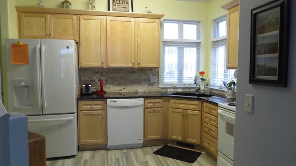 A kitchen with wooden cabinets, a refrigerator, a dishwasher, and a window with blinds. - Lovely townhome on a pond in Plantation East - 10 Crane (Lewes)