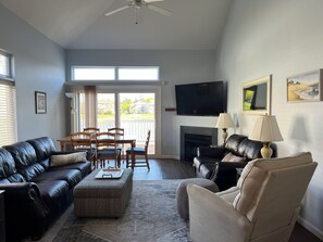 Una sala de estar con chimenea, televisor y comedor con vistas a través de puertas de vidrio.