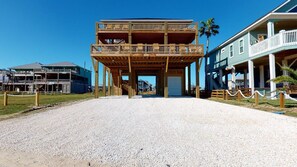A two-story wooden building with a balcony, a gravel driveway, and a clear blue sky.