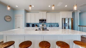 A kitchen with white cabinets, a large island with stools, stainless steel appliances, and pendant lighting.