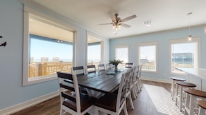 A dining area with a long table, white chairs, and a ceiling fan.