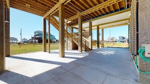 Edifício em construção com vigas de madeira aparentes, piso de concreto e escada que leva a um andar superior.