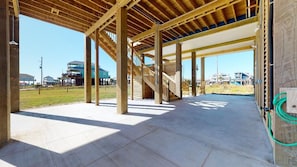 A building under construction with exposed wooden beams, a concrete floor, and a staircase leading to an upper level.