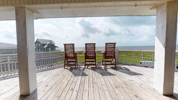A wooden deck with three chairs facing a view of the ocean and a house.