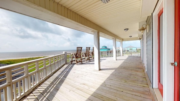 A covered wooden deck with chairs, a railing, and a view of the ocean.