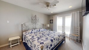 A bedroom with a bed, a ceiling fan, a nightstand, a chair, and a window with curtains.
