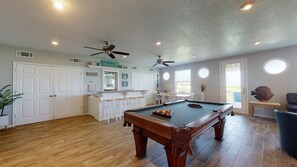 A spacious room with a pool table, ceiling fans, and a bar area.