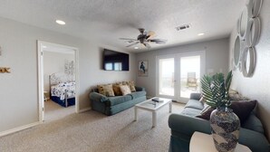 A living room with a ceiling fan, a sofa, a coffee table, and a TV mounted on the wall.