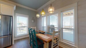 Una cocina con una mesa de madera, sillas color turquesa, un refrigerador y tres lámparas colgantes.