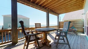 A wooden deck with a table and chairs, overlooking a beach.