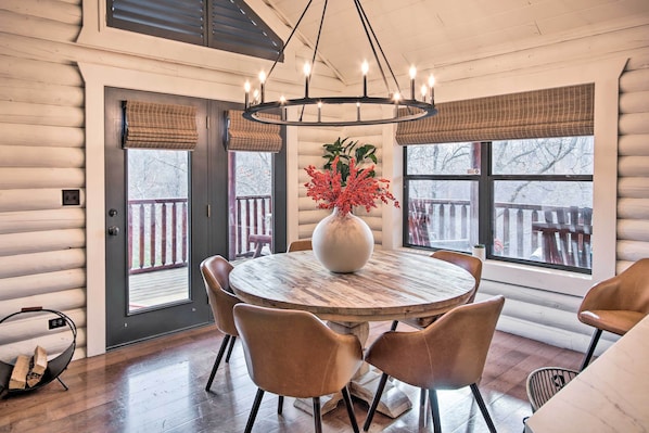 A wooden dining table with six chairs, a large vase with red flowers, and a chandelier.