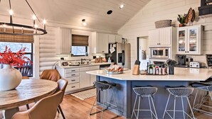 Una cocina moderna con armarios blancos, una isla central con taburetes y un comedor con una mesa redonda y sillas.