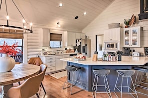 Una cocina moderna con armarios blancos, una isla central con taburetes y un comedor con una mesa redonda y sillas.