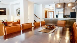 Un vaste salon doté d’un plancher en bois, de fauteuils en cuir, d’une table basse et d’un coin cuisine avec des appareils en acier inoxydable.