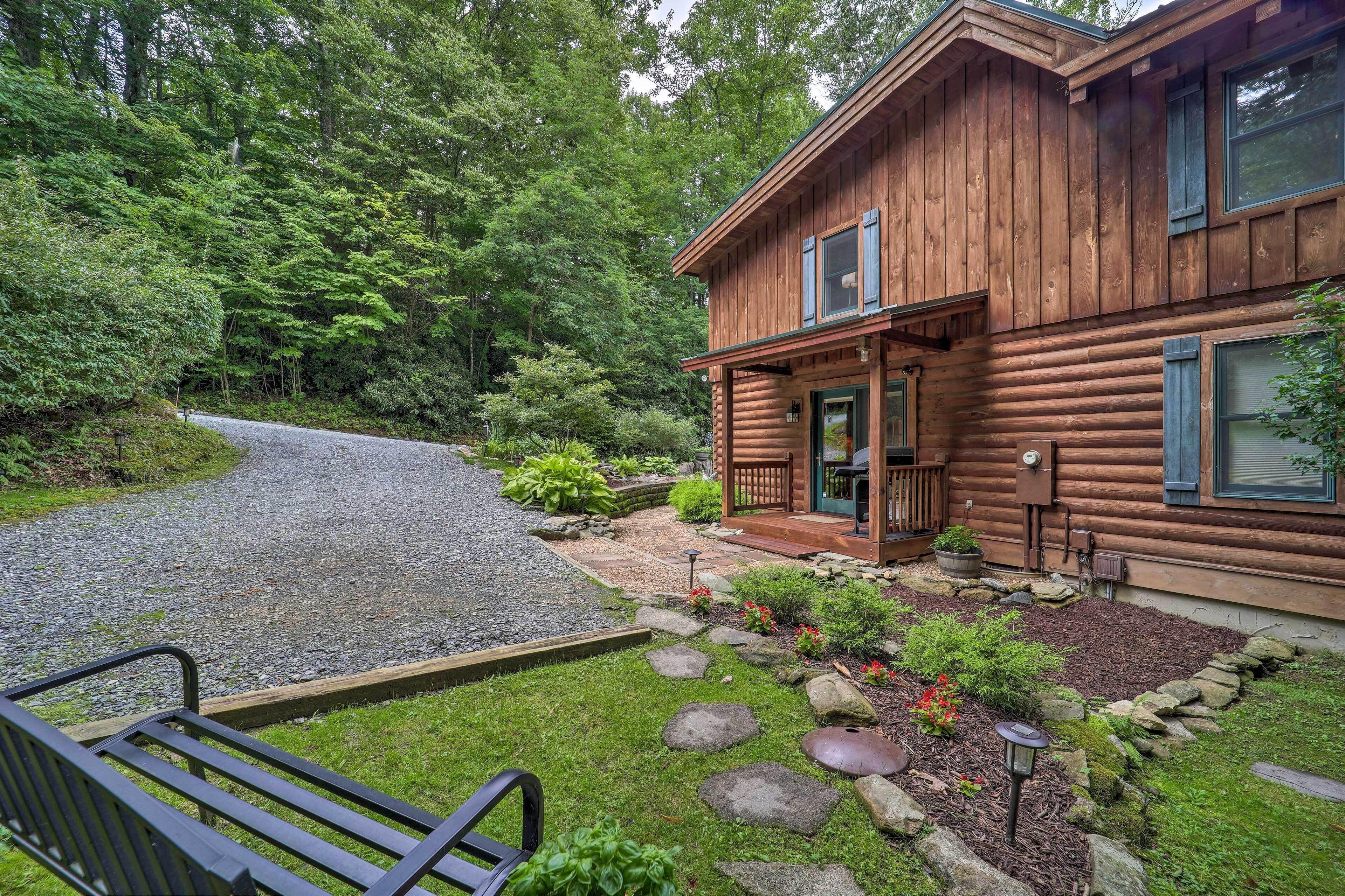 A log cabin with a porch, a gravel driveway, and a garden with rocks and plants.