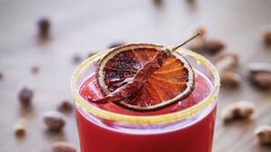 Un vaso de bebida roja adornado con una rodaja de naranja deshidratada sobre una superficie de madera.