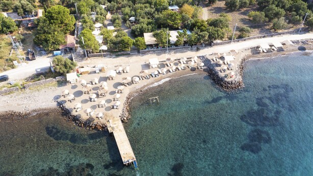 Vista aérea de una zona costera con un muelle que se adentra en el mar, rodeada de servicios para la playa, como tumbonas y sombrillas.
