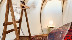 Una tienda con una escalera de madera, una cama con una manta estampada y una pequeña mesa con una lámpara.