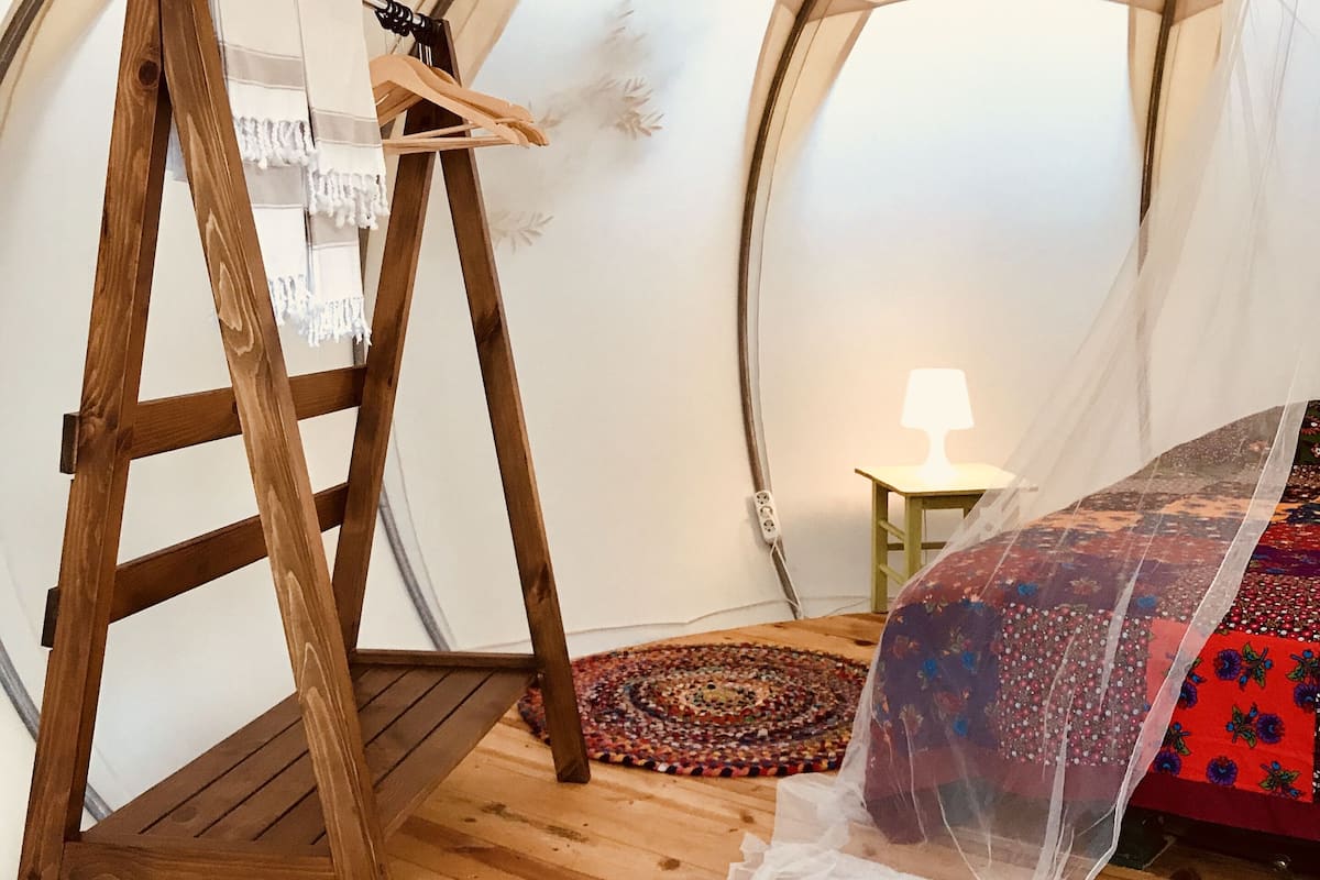 A tent with a wooden ladder, a bed with a patterned blanket, and a small table with a lamp.