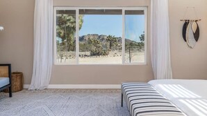 A bedroom with a large window, a bed, a bedside table, and a wall-mounted decoration. - @Marbella Lane -  Charming Tranquil Hideaway (Yucca Valley)