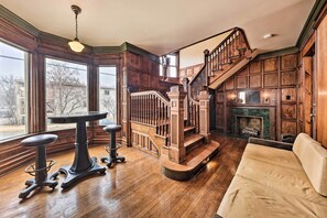 Una habitación amplia con escalera de madera, chimenea y ventanas grandes.