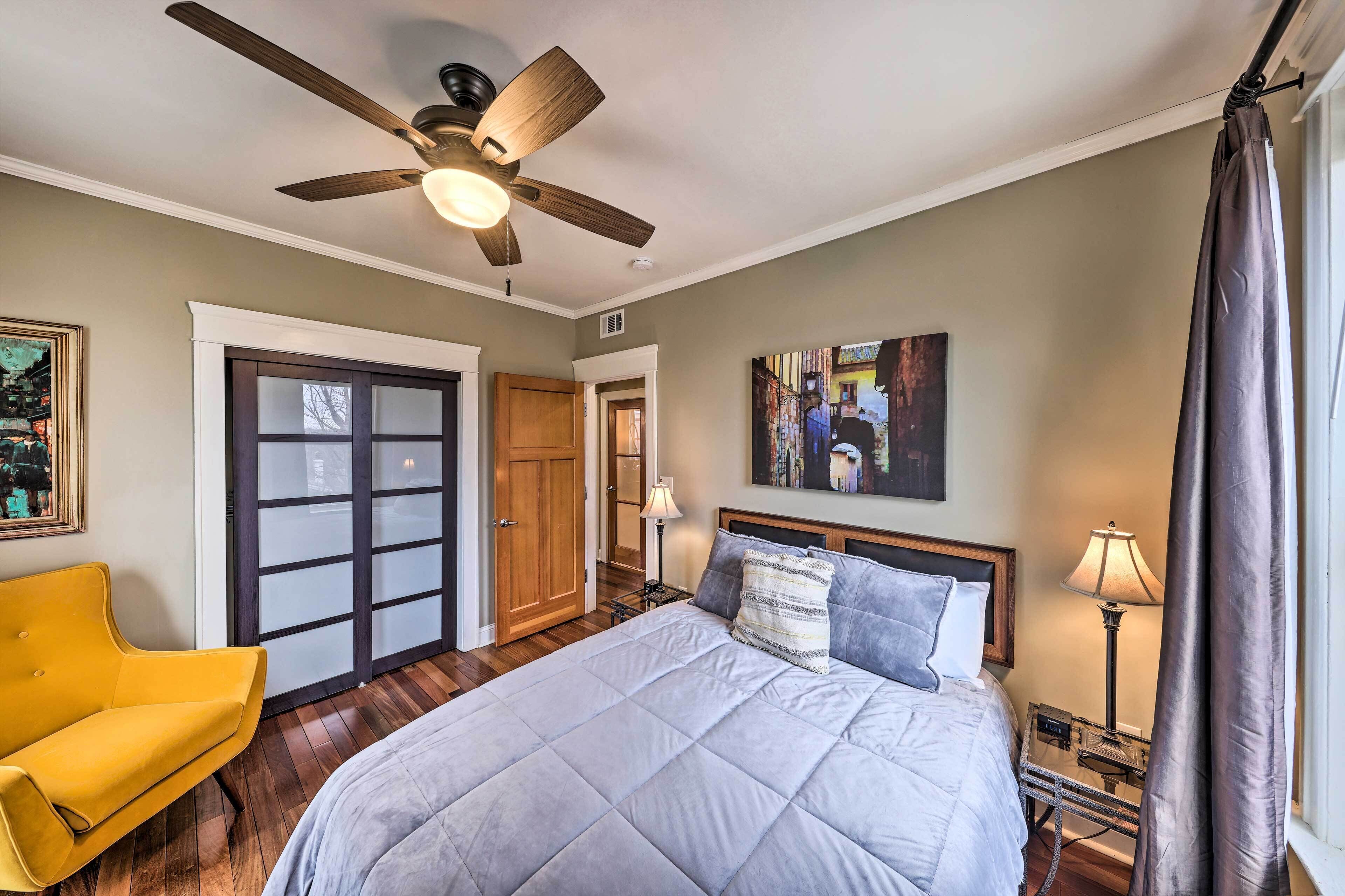 A bedroom with a bed, a ceiling fan, a nightstand with a lamp, a yellow chair, and a door with frosted glass panels.