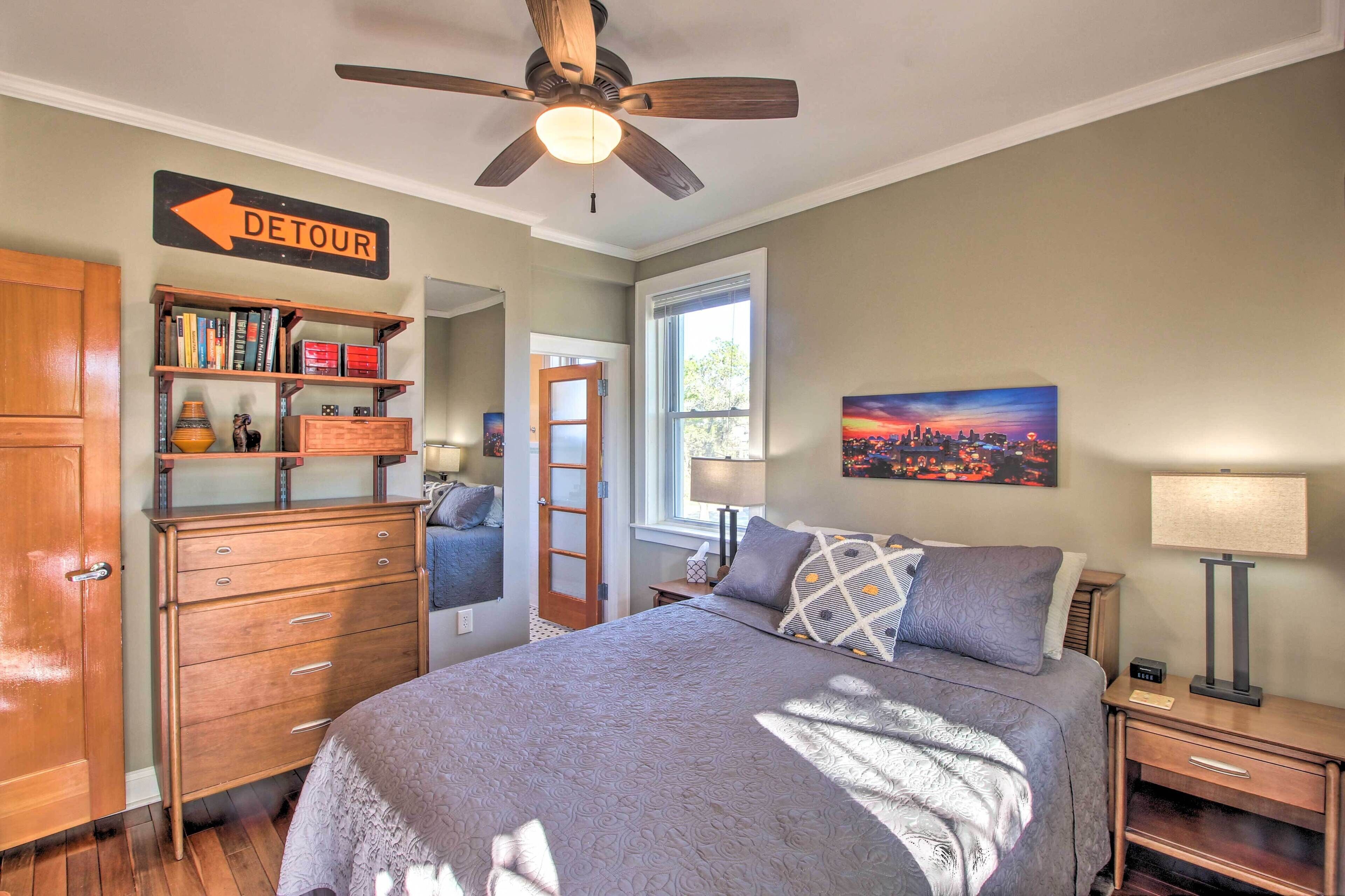 Um quarto com uma cama, mesa de cabeceira, abajur, estante de livros, guarda-roupa, porta e um quadro na parede.