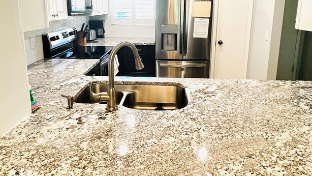 A kitchen with white cabinets, stainless steel appliances, a granite countertop, and two wooden stools. - Ocean view 2 bedroom, 2 bath flat. (Saint Augustine)