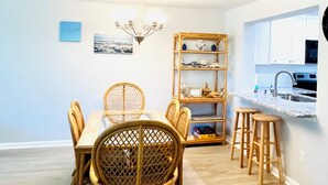 A dining area with a table and chairs, a chandelier, a bookshelf, and a kitchen area with a sink and cabinets. - Ocean view 2 bedroom, 2 bath flat. (Saint Augustine)