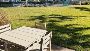 An outdoor patio area with a table and chairs, a grassy lawn, and a building in the background. - Ocean view 2 bedroom, 2 bath flat. (Saint Augustine)