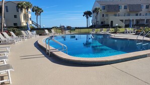 A swimming pool with a curved edge, surrounded by lounge chairs and a fence. - Ocean view 2 bedroom, 2 bath flat. (Saint Augustine)